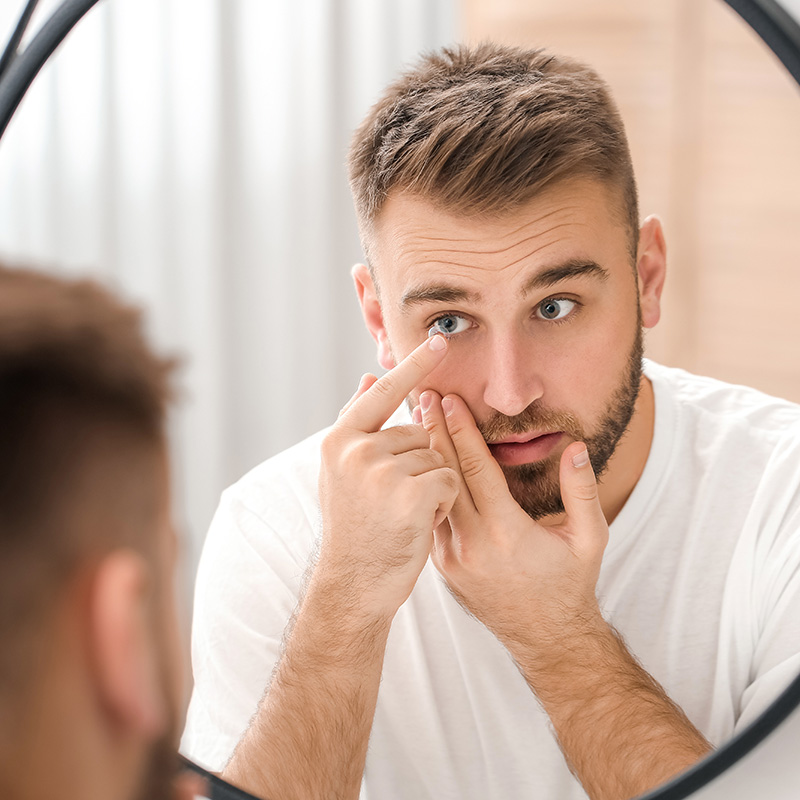 Young man putting in contact lenses near mirror