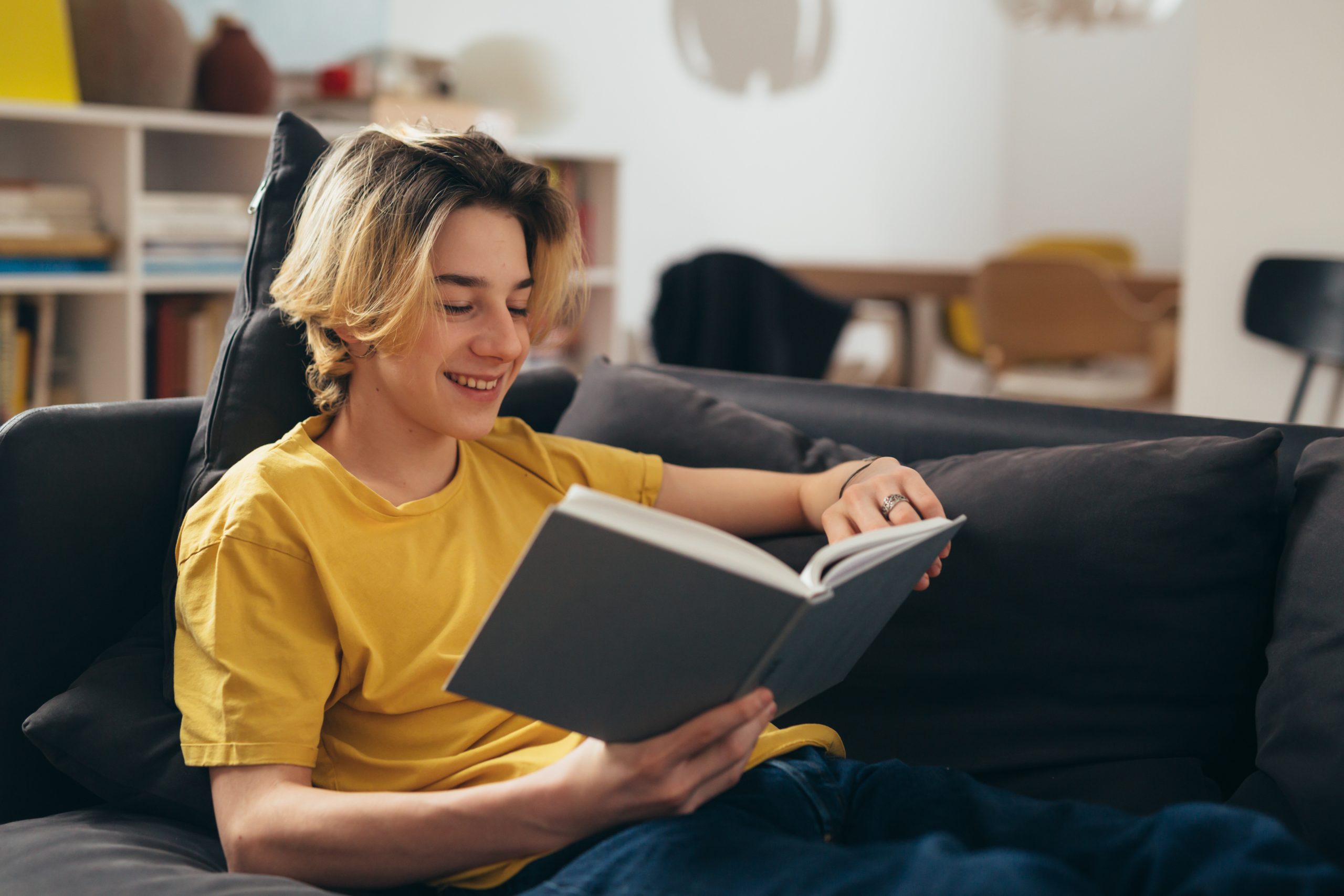 teenager reading book while sitting on couch at home