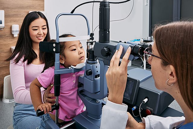 Cute little Asian girl getting eye exam at ophthalmology clinic with optometrist. Checking retina of female child eye, ophthalmology for children