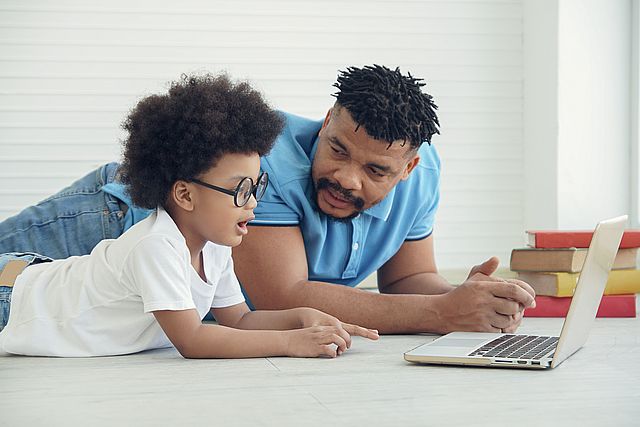 An African American family father and little son wearing eye glasses lying with laptop on a white background