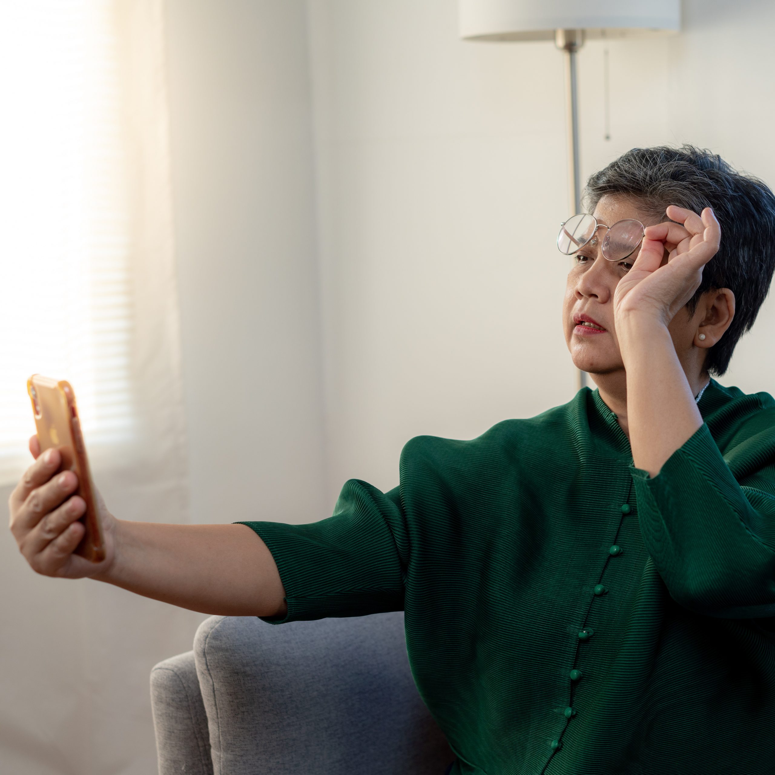 An elderly person raises his glasses to try to focus on his phone