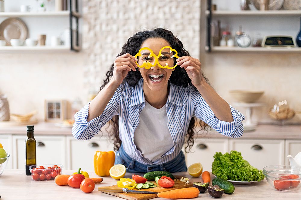 Excited woman making glasses of sweet pepper, having fun and playing with food while cooking fresh salad