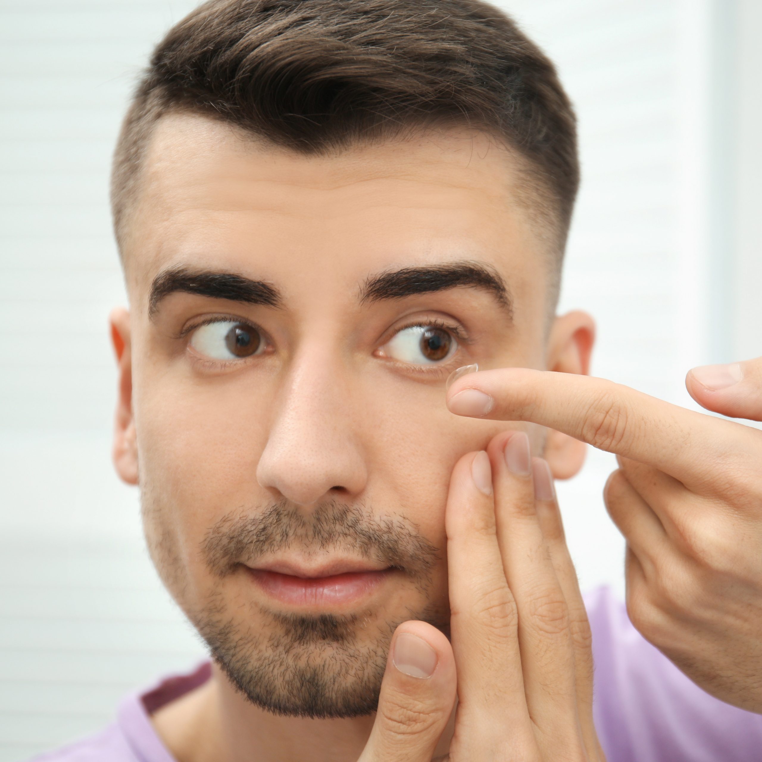 young man holding contact lens near eyey