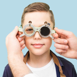 close up of young boy covering one eye in front of eye chart