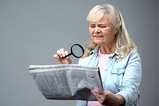 senior with magnifiying glass reading newspaper
