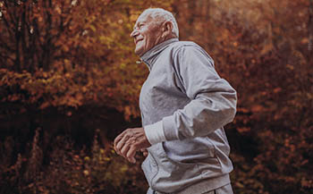 Senior Runner In Nature. Elderly Sporty Man Running In Forest Du