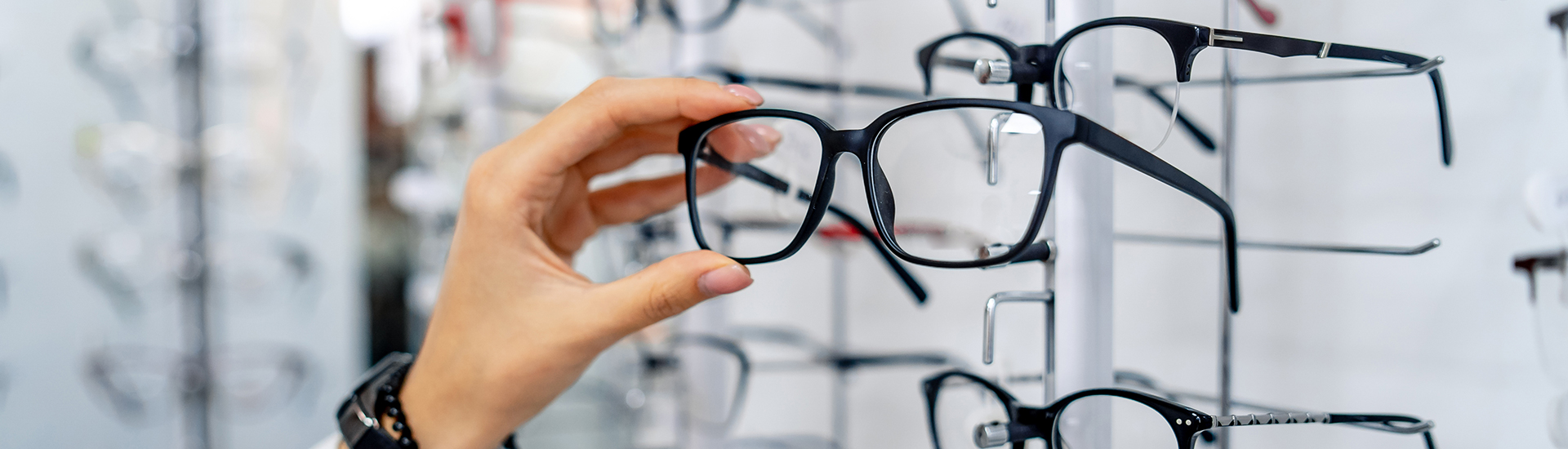 Row-of-glasses-at-an-opticians.-Eyeglasses-shop.-Stand-with-glasses-in-the-store-of-optics.-Woman-chooses-spectacles.-Eyesight-correction