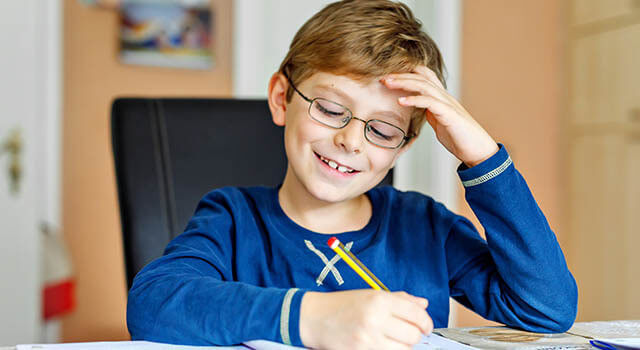 boy in blue shirt wearing glasses writing with a pencil