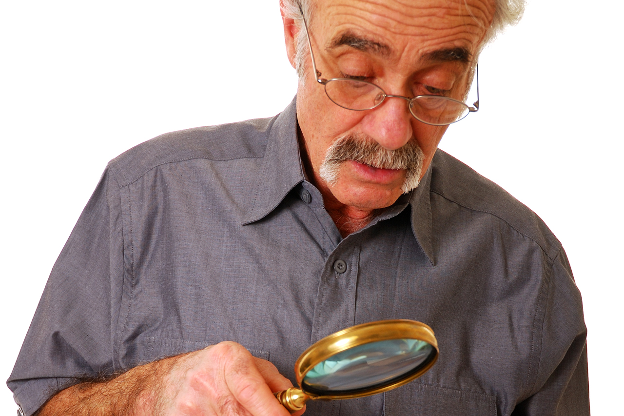 Man wearing eyeglasses, using magnifying glass