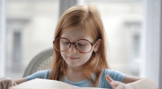 little girl wearing glasses reading a book 640×350